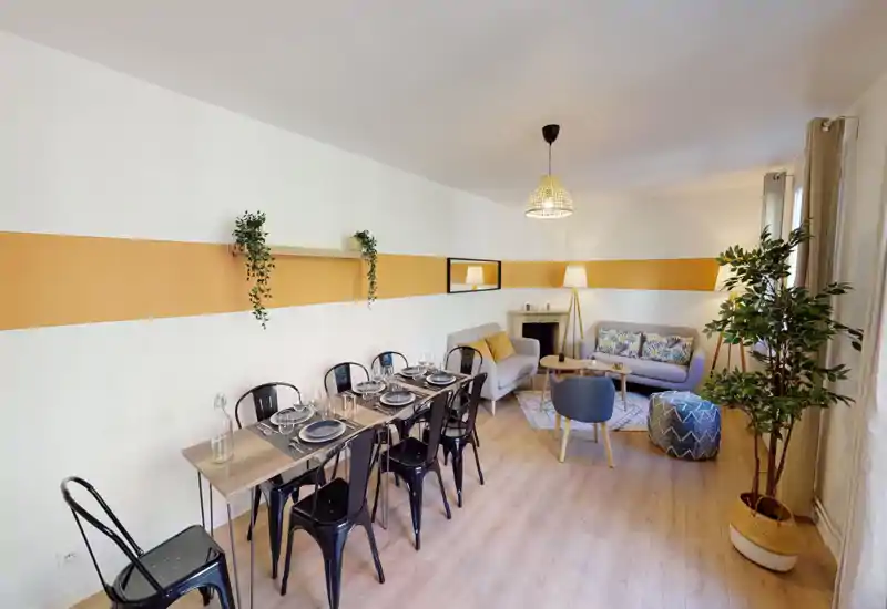 Zona giorno luminosa e moderna con tavolo da pranzo apparecchiato, due divani comodi, cuscini decorativi e piante che rendono l'ambiente accogliente.