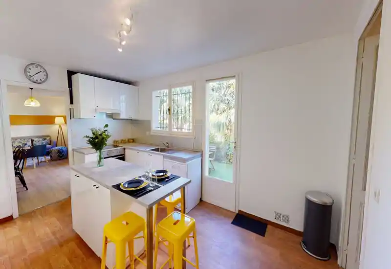 Cucina moderna e luminosa con mobili bianchi, isola con piano per la colazione per due persone e porta sul giardino — elegante e pronta all'uso.