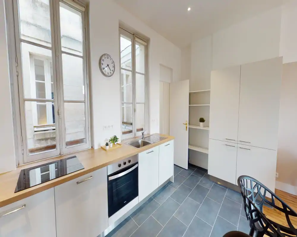 Cuisine moderne et lumineuse avec grandes fenêtres, four encastré et plaque à induction, plan de travail en bois et évier intégré — espace propre et fonctionnel idéal pour une location.