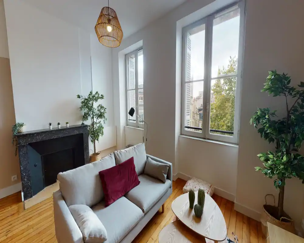 Salon lumineux et élégant avec un canapé confortable, coussins décoratifs, plantes d'intérieur et grandes fenêtres laissant entrer une belle lumière naturelle.