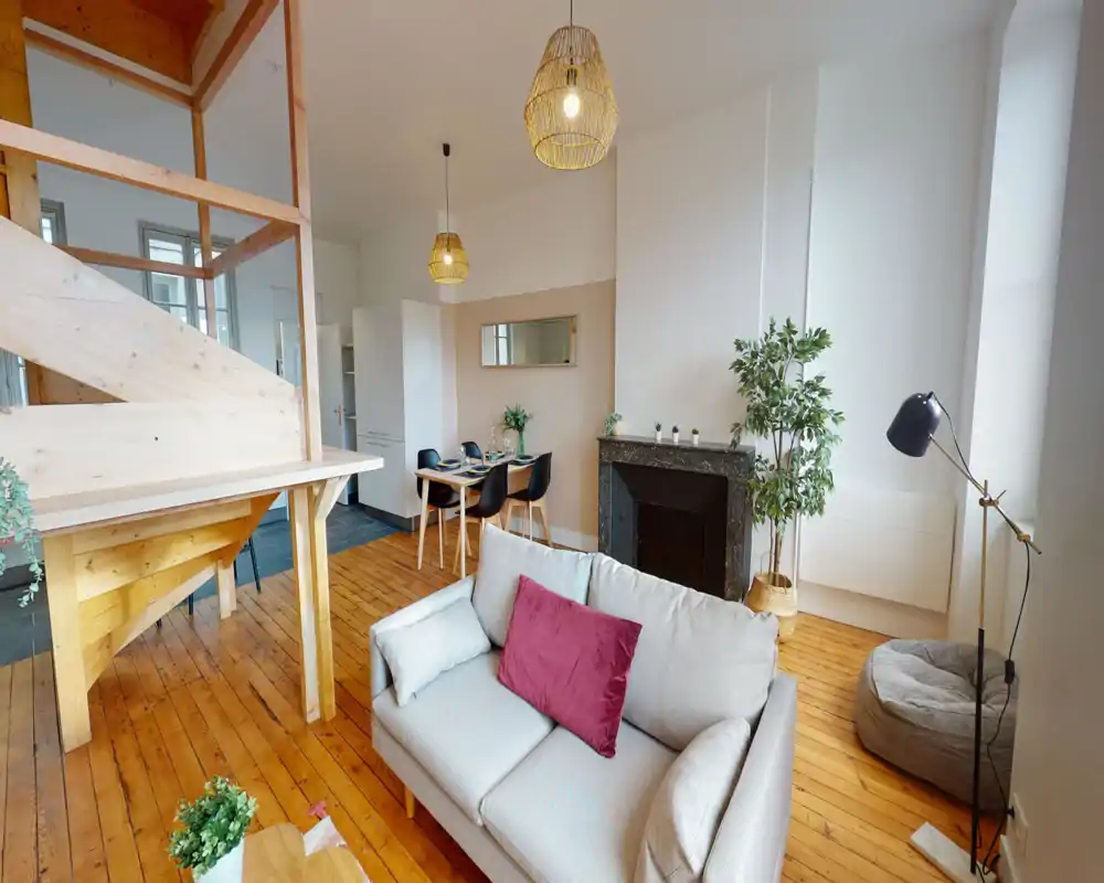 Espace de vie lumineux et aménagé avec canapé confortable, coussins décoratifs, cheminée, table à manger et parquet chaleureux — un salon ouvert et accueillant.