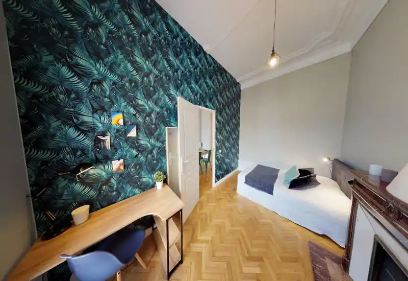 Bright, stylish bedroom with a single bed, decorative tropical-pattern accent wall, wooden parquet floor and a small desk—ideal for a comfortable solo stay.