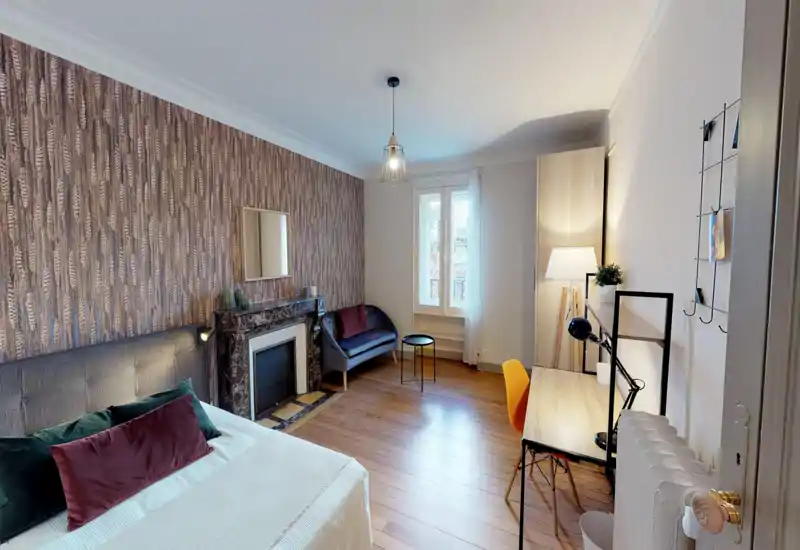 Chambre spacieuse et élégante avec grand lit bien visible, parquet, papier peint décoratif et coin salon près de la fenêtre — lumineuse et accueillante.