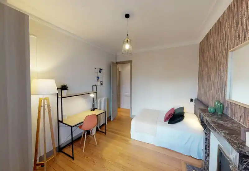 Chambre lumineuse et bien décorée avec lit simple, coussins décoratifs et parquet; un bureau avec lampe offre un espace fonctionnel et chaleureux.