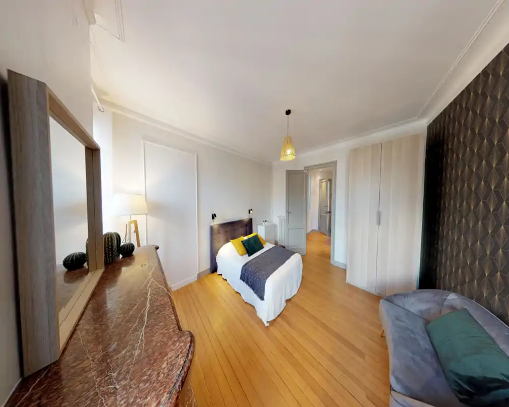 Bright, stylish bedroom with a comfortable double bed, decorative cushions and a warm wooden floor. Neutral walls and patterned accent wallpaper create a calm, modern atmosphere.