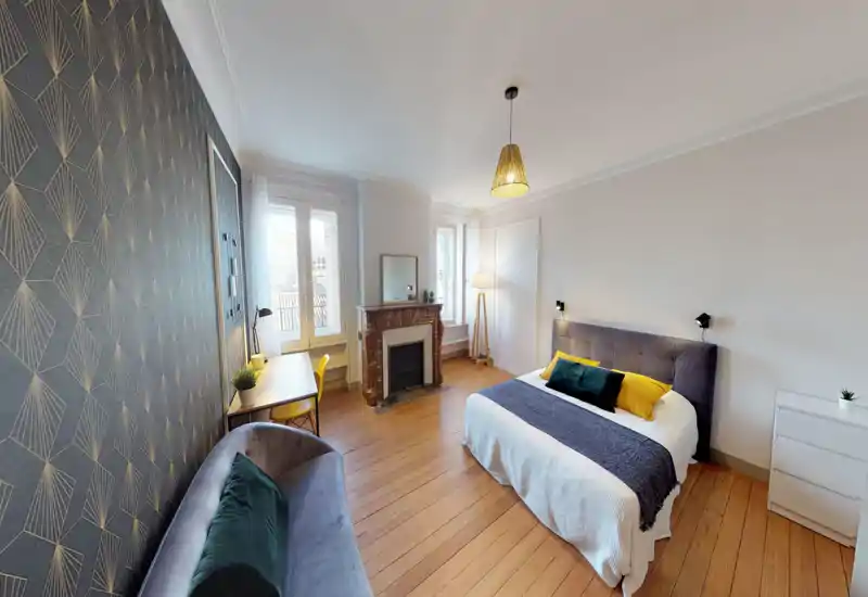 Bright, well-styled bedroom with a comfortable double bed, decorative pillows and throws, a desk by the window and a cozy seating area. Large windows and tasteful wallpaper create an airy, inviting atmosphere perfect for rentals.