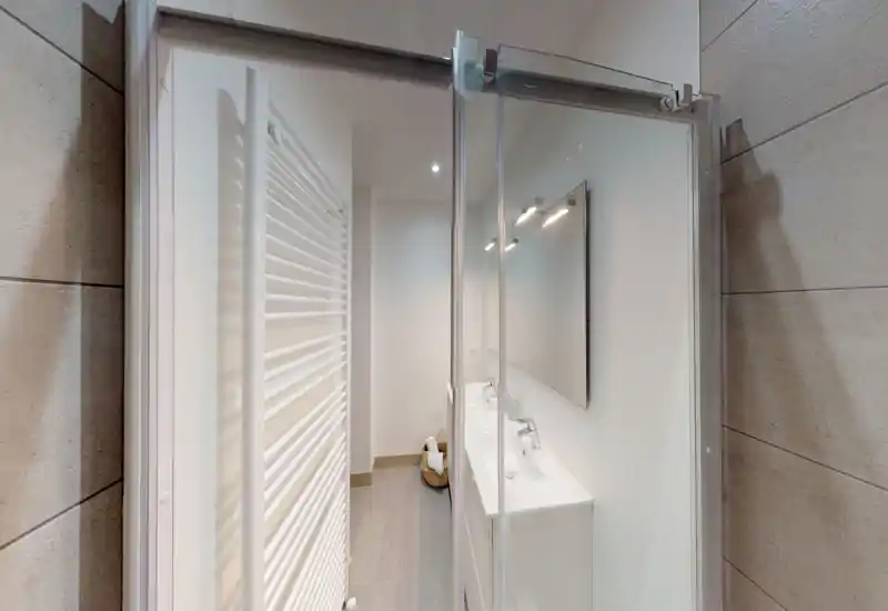 Bagno moderno e luminoso con doppio lavabo, grande specchio e termoarredo verticale; linee pulite e piastrelle neutre creano un'atmosfera contemporanea e rilassante.