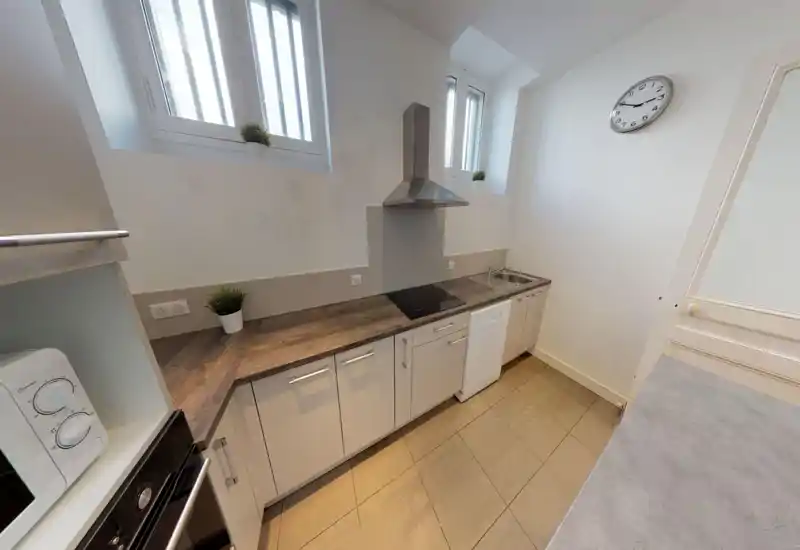 Cucina compatta e luminosa con piano in effetto legno, piano cottura integrato con cappa, lavello, lavastoviglie e piccole piante decorative; finiture moderne e pulite, ideale per un appartamento in città.
