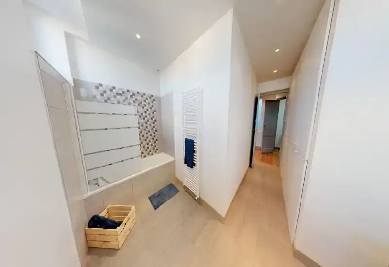 Bagno moderno e luminoso con vasca/doccia piastrellata, parete con piastrelle decorative a mosaico e scaldasalviette. Stile pulito e minimale con buona illuminazione dall’alto.