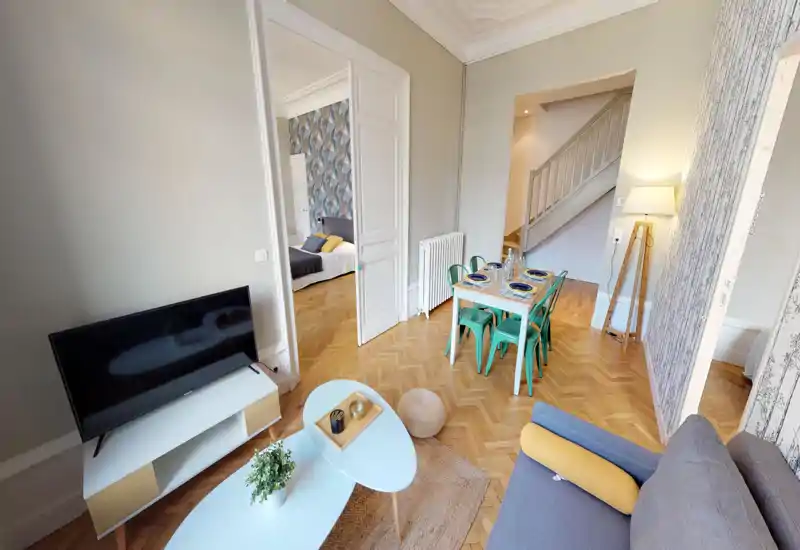 Séjour lumineux et élégant avec canapé confortable, table basse, meuble TV et une petite table à manger. Parquet chaleureux et décor agréable pour une ambiance accueillante.