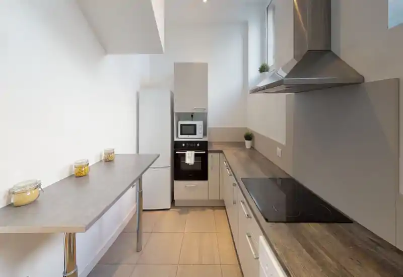 Cucina compatta e moderna con piani in legno, forno incassato, piano a induzione e cappa in acciaio. Layout luminoso e pulito con piante e vasetti che aggiungono un tocco accogliente.