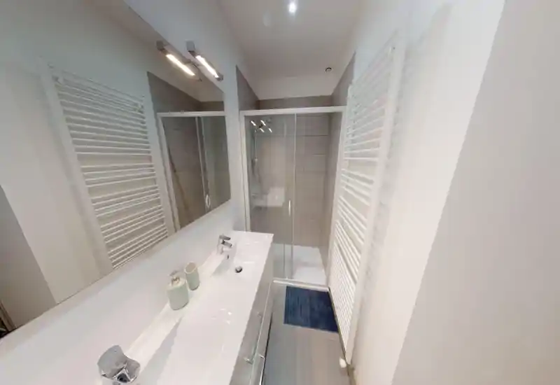 Bagno moderno e compatto con box doccia in vetro, termoarredo a parete, lavabo bianco con rubinetteria cromata e un grande specchio che dona un aspetto pulito e luminoso.