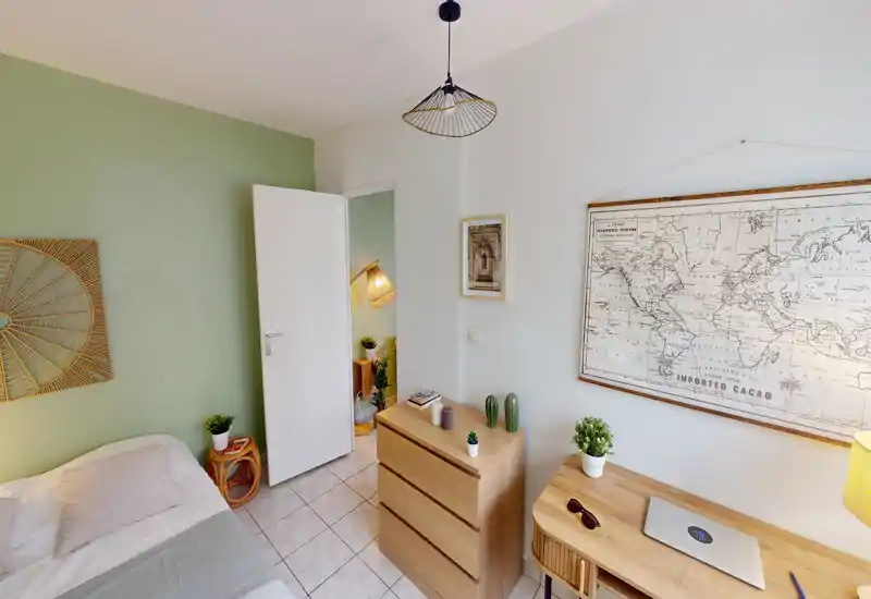 Chambre compacte et bien décorée avec lit simple, commode et bureau en bois, mur vert en accent et carte murale. Lumineuse et cosy, parfaite pour une location courte durée.