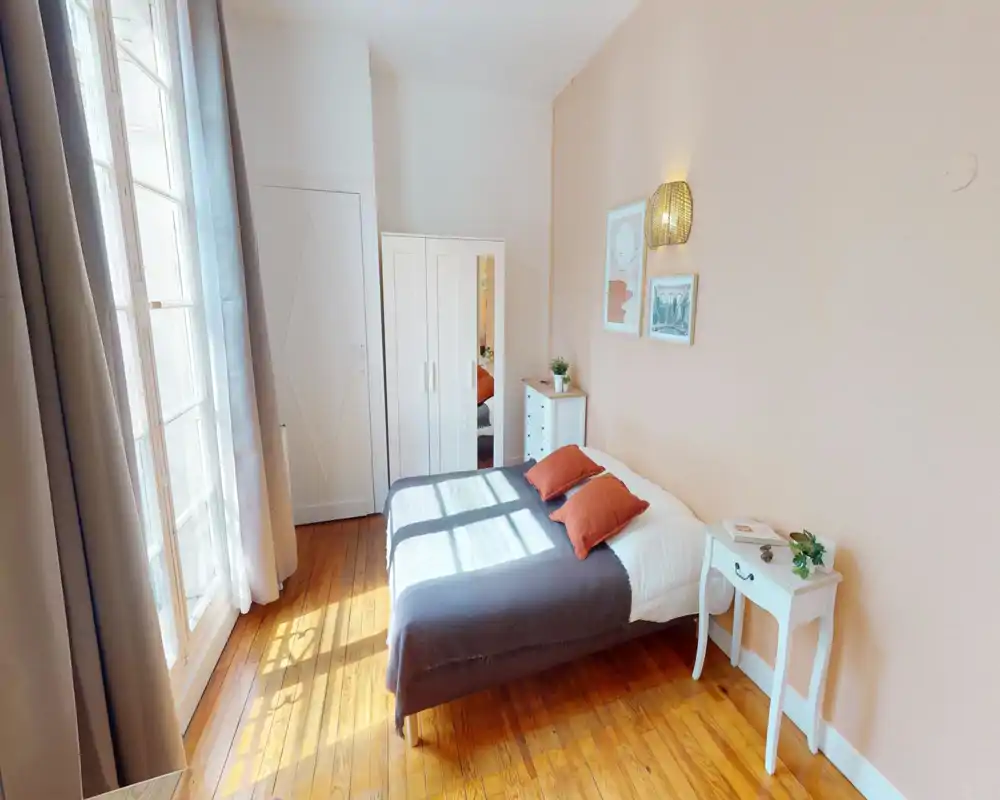 Camera da letto luminosa con letto matrimoniale in biancheria neutra e cuscini color ruggine, pavimento in legno, armadio e comodini — accogliente, ben illuminata e dallo stile semplice.