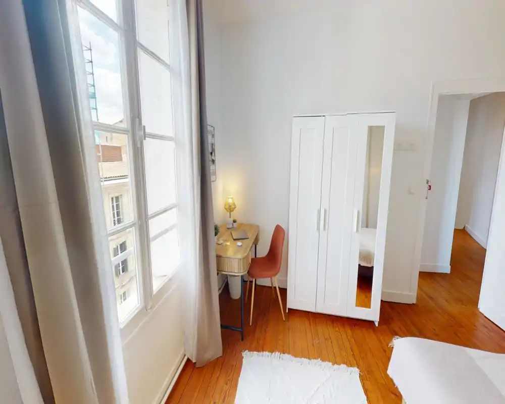 Angolo camera luminoso e accogliente con grande finestra, scrivania compatta e armadio; pavimenti in legno e tessuti morbidi creano un’atmosfera calda.