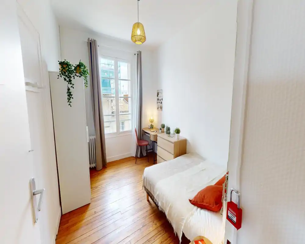 Camera da letto luminosa e curata con letto singolo, pavimenti in legno e una piccola scrivania vicino alla finestra — ambiente accogliente ideale per una persona.