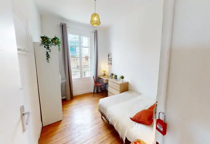 Camera da letto luminosa e curata con letto singolo, pavimenti in legno e una piccola scrivania vicino alla finestra — ambiente accogliente ideale per una persona.