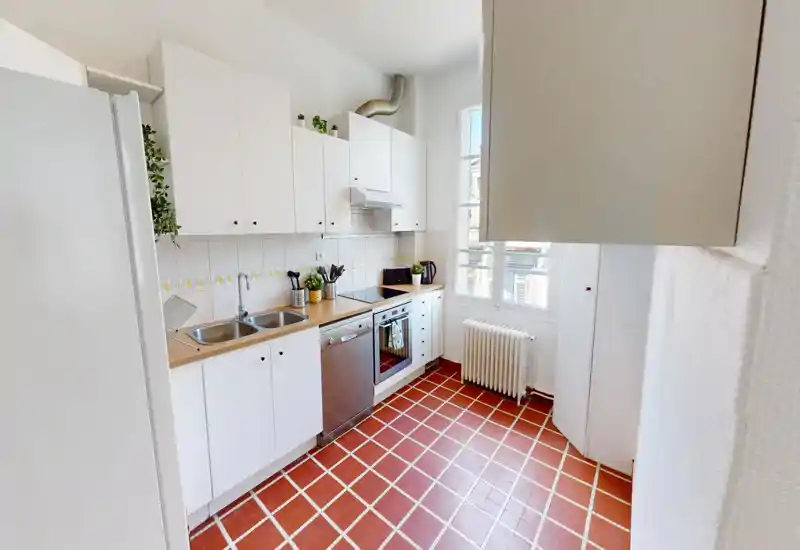 Cucina luminosa e ben attrezzata con mobili bianchi, forno e lavastoviglie incassati, doppio lavello e ampia finestra che garantisce luce naturale — spazio pulito e funzionale ideale per affitti.