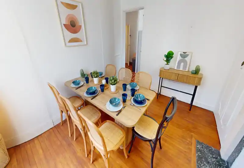 Sala da pranzo luminosa e arredata con un tavolo in legno apparecchiato per sei, sedie in midollino e piante decorative che creano un'atmosfera accogliente.