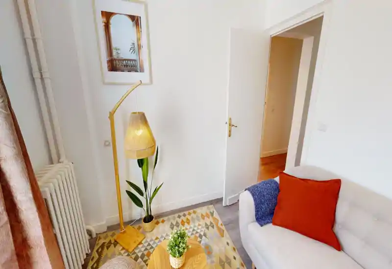Area soggiorno accogliente con divano neutro, cuscini colorati, tappeto con motivi e una lampada da terra calda; angolo luminoso e ben arredato ideale per rilassarsi.