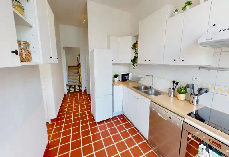 Cucina luminosa e ben attrezzata con armadi bianchi, piano in legno, lavello doppio, lavastoviglie e piano cottura elettronico. Ambiente ordinato e decorato con piccole piante e utensili, perfetto per foto di affitto.