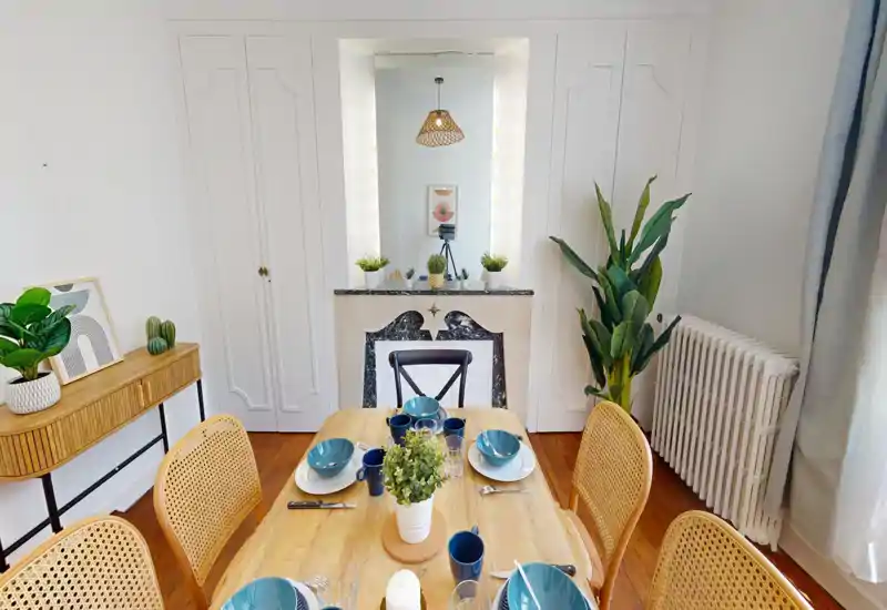 Zona pranzo luminosa e curata con tavolo in legno apparecchiato per quattro, sedie con schienale in giunco e piante decorative che creano un ambiente accogliente.