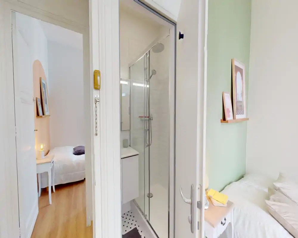 Camera da letto luminosa e compatta con letto ben rifatto, comodino con lampada e stampe decorative su una parete verde chiaro — accogliente e ben illuminata, ideale per un annuncio.