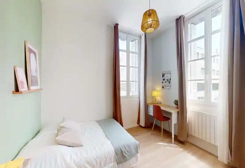 Camera da letto luminosa e ben arredata con letto completo, ampie finestre e una scrivania compatta. La luce naturale e gli accenti caldi rendono la stanza accogliente e adatta agli affitti brevi.