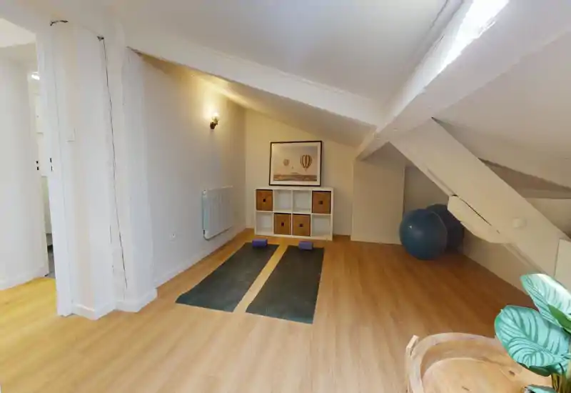 Airy attic living space staged for relaxation and yoga: wooden floors, two yoga mats with blocks, wicker storage cube shelf and framed wall art under a sloped ceiling.