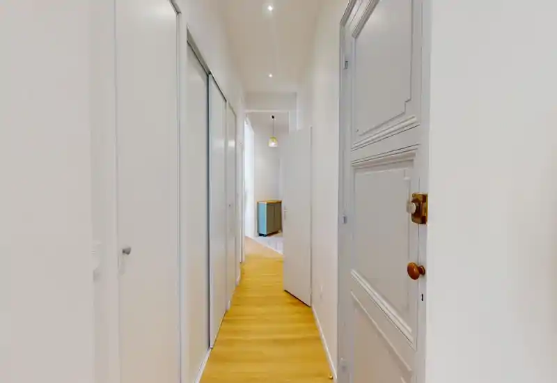 Corridoio luminoso e pulito con pavimento in legno e armadi a muro; piccolo lampadario moderno visibile verso l'interno.