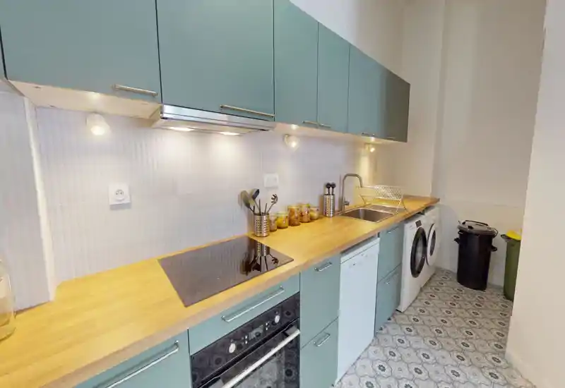 Cucina moderna a corridoio con piano in legno, pensili turchesi, forno e piano cottura integrati, lavello con scolapiatti e illuminazione sotto i mobili; pratica, ordinata e ben illuminata.