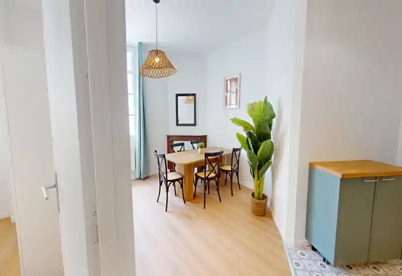 Zona pranzo luminosa e curata con tavolo in legno, quattro sedie e un lampadario decorativo; piante e luce naturale rendono l’ambiente accogliente.