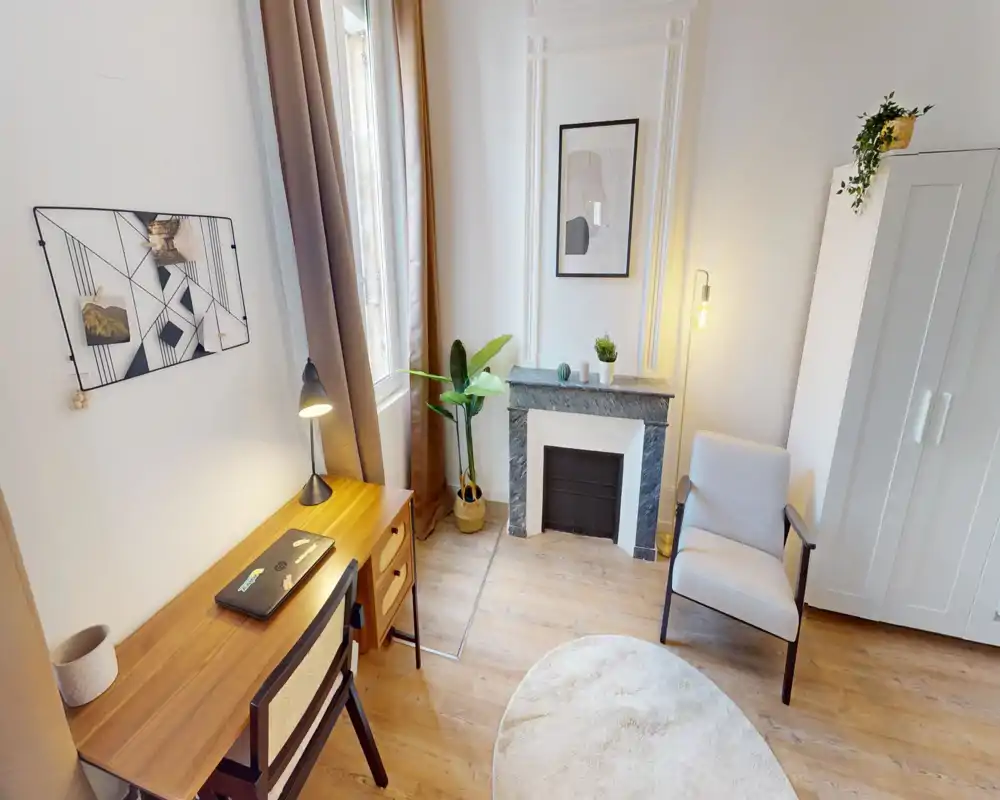 Coin chambre lumineux et soigné avec bureau, fauteuil et cheminée décorative ; grande fenêtre et lampes chaleureuses pour une ambiance cosy.
