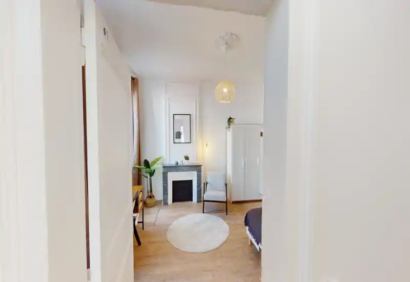Chambre lumineuse et élégante avec tapis rond, fauteuil, armoire et cheminée décorative ; tons neutres et plantes pour une ambiance apaisante.