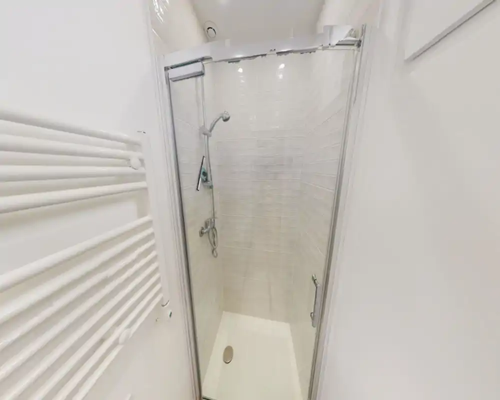 Douche moderne et compacte avec porte vitrée, murs carrelés, robinetterie chromée et bac de douche blanc. Intérieur propre, lumineux et minimaliste, parfait pour optimiser l'espace.