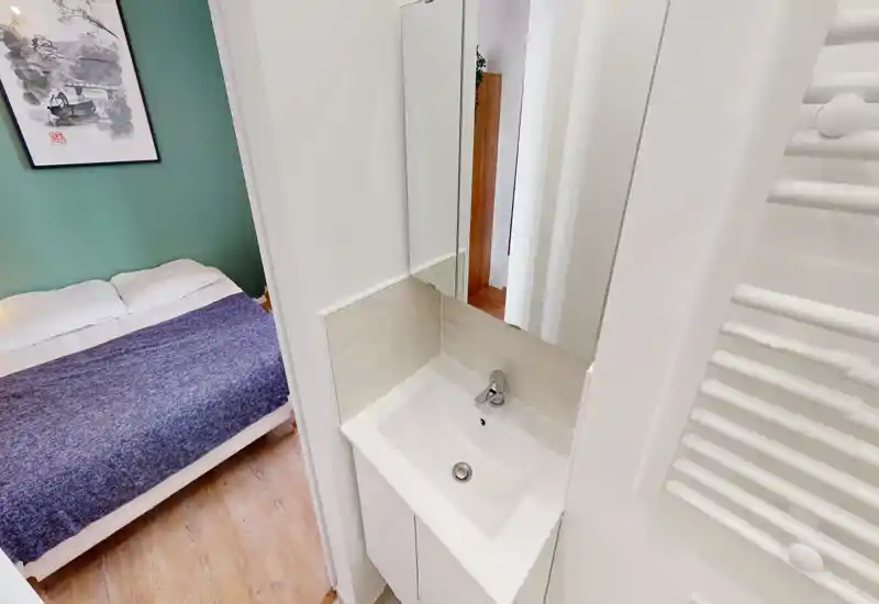 Coin chambre lumineux et soigné avec un lit double, des oreillers moelleux et une couverture bleu marine texturée sur un mur vert; un cadre apporte du caractère.