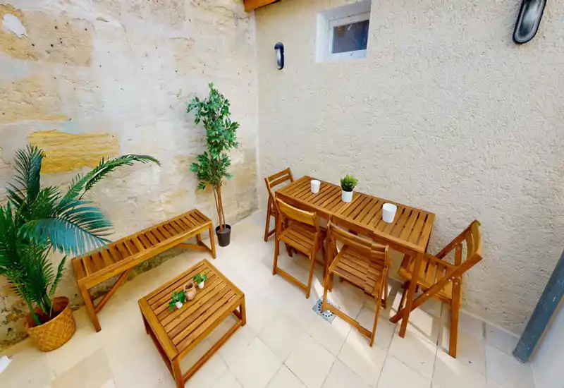 Piccolo cortile soleggiato con set da pranzo in legno, panca e piante in vaso — un patio privato e luminoso ideale per pasti rilassati o un caffè.