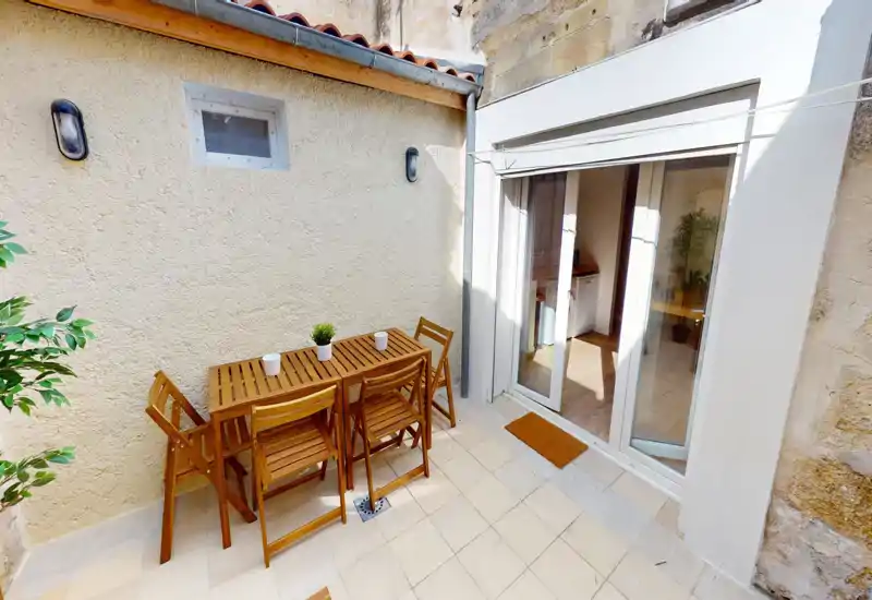Terrazza privata soleggiata con tavolo e sedie pieghevoli in legno, pavimento piastrellato e accesso diretto tramite porte scorrevoli in vetro—perfetta per il caffè mattutino.