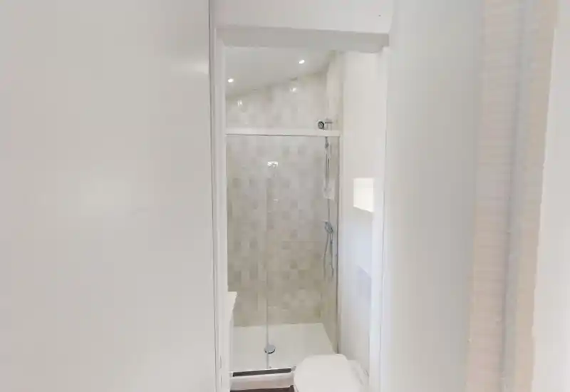 Bagno compatto e moderno con doccia piastrellata, porta scorrevole in vetro e WC a muro; piastrelle neutre e faretti a incasso creano un aspetto pulito e contemporaneo.