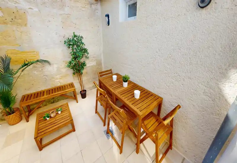 Piccola terrazza soleggiata con tavolo e sedie in legno e piante in vaso — perfetta per colazioni o aperitivi in un cortile privato.