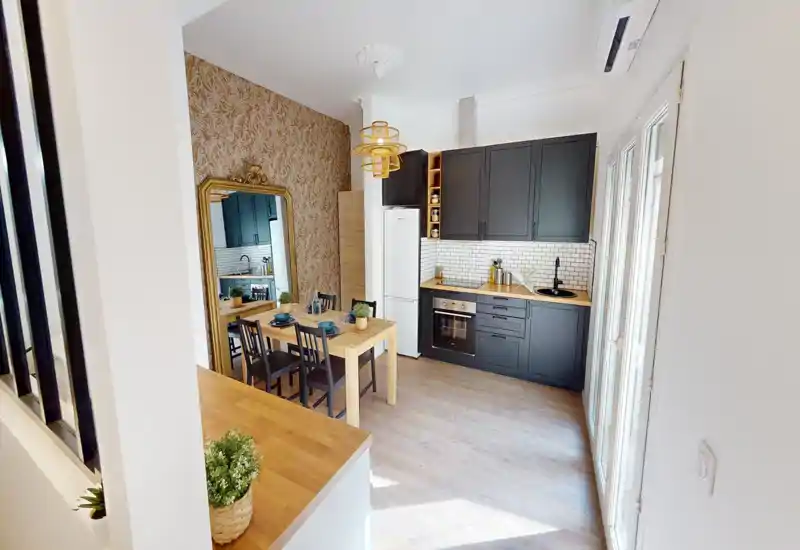 Cucina moderna e compatta con mobili scuri, piani in legno e paraschizzi piastrellato; tavolo da pranzo per quattro e ampie finestre che illuminano bene l'ambiente.