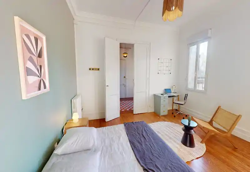 Sunny, styled bedroom with a comfortable double bed, wooden floors, a small desk by the window and minimalist decor creating a calm atmosphere.