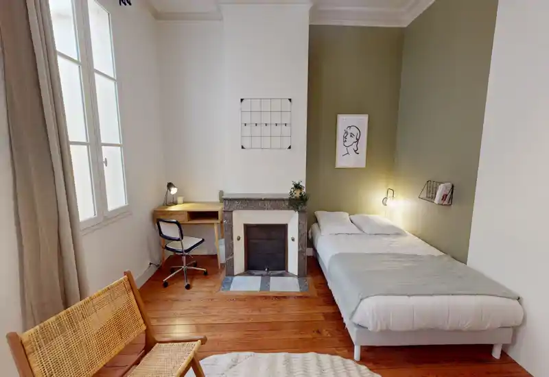 Camera da letto luminosa e di stile con letto matrimoniale contro una parete verde, pavimenti in legno, una scrivania vicino alla finestra e dettagli decorativi caldi.