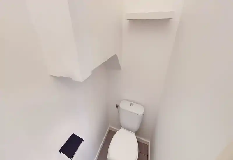 Stanza wc compatta con visione ravvicinata del water bianco e pareti bianche semplici; luminosa, pulita e minimale.