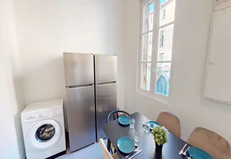 Cucina compatta con angolo pranzo per quattro persone, frigorifero in acciaio inox e lavatrice accanto. Ampia finestra che dona molta luce naturale e un ambiente accogliente.