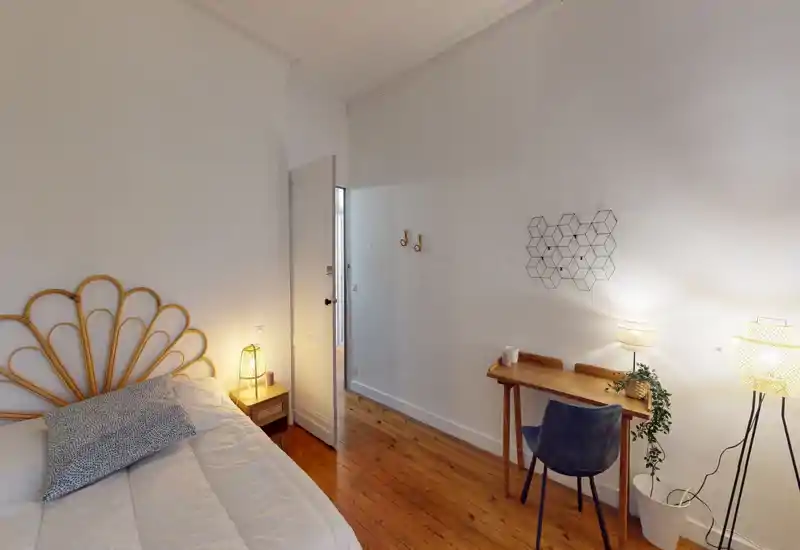Chambre lumineuse et chaleureuse avec tête de lit en rotin, parquet bois et un petit coin bureau avec lampe — idéale pour un séjour confortable.