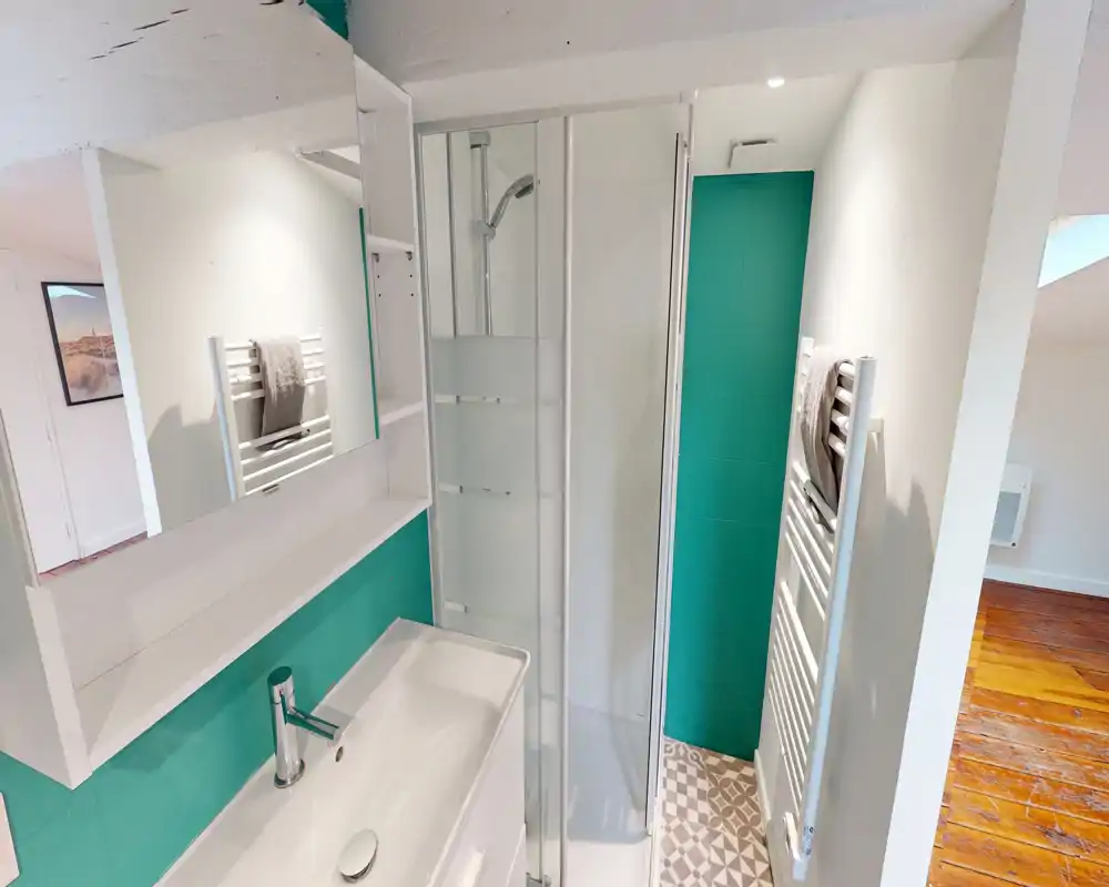 Bagno moderno e compatto con cabina doccia in vetro, lavabo bianco e parete d'accento turchese; piastrelle a motivo e scalda-asciugamani per comfort e stile.