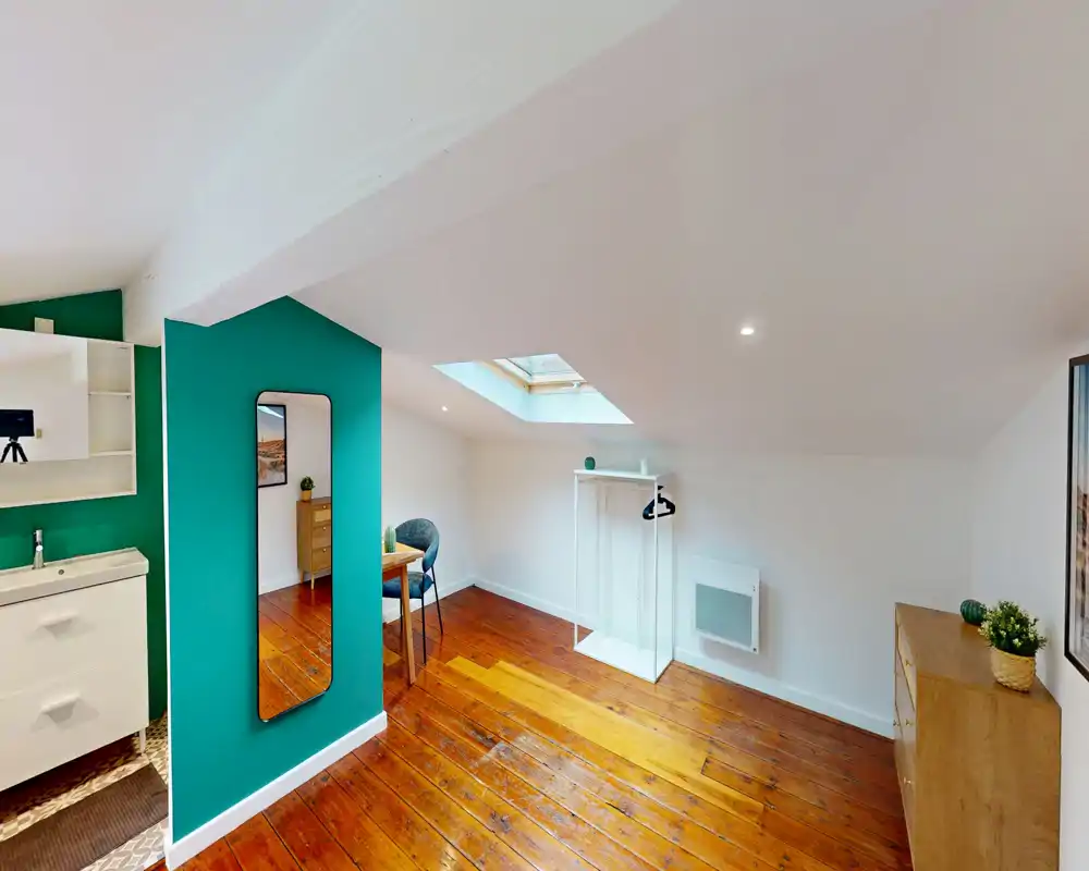 Luminoso ambiente in mansarda con soffitto inclinato, finestra a tetto e pavimento in legno caldo; arredamento minimale con sedia, piccolo tavolo e attaccapanni aperto.
