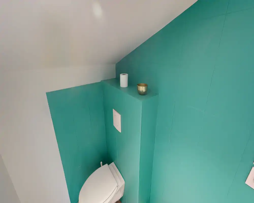 Piccolo bagno moderno ad angolo con wc a muro e pareti piastrellate turchesi; stile minimale e buona illuminazione.