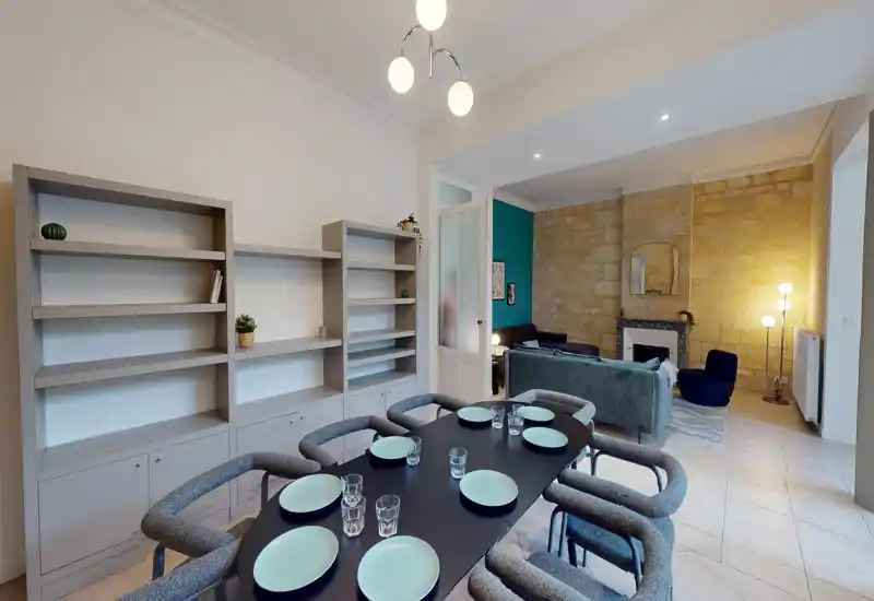 Ampio e moderno ambiente giorno con grande tavolo da pranzo per sei, divano confortevole, parete in pietra a vista e illuminazione soffusa — perfetto per pranzi in compagnia e relax.